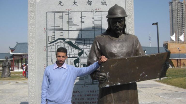 ইখতিয়ার ‍উদ্দিনের ভাস্কর্যকে পাশে নিয়ে দাঁড়ানো মূল লেখক, পেছনে ইখতিয়ার ‍উদ্দিনের প্রস্তুত করা মানচিত্র